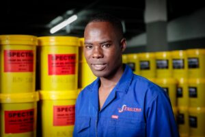 Home 1 Spectra Oil employee standing beside stacked drums of Spectra industrial lubricants